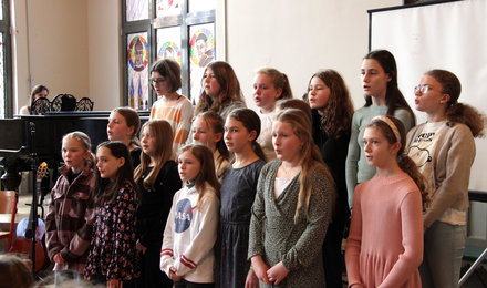 Mädchenchor singt und wird von einer Frau am Flügel begleitet