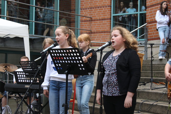 Zwei Schülerinnen singen und weitere spielen Instrumente