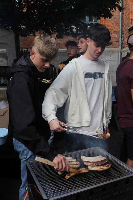Zwei Schüler grillen Wurst und beide halten eine Zange in der Hand