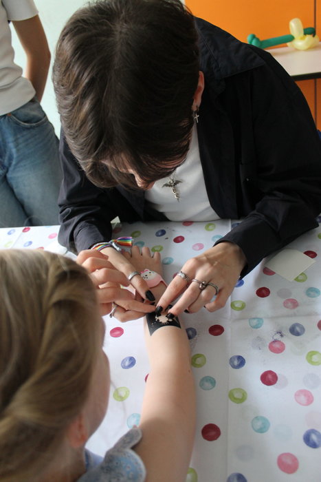 Einem Mädchen wird von einer dunkelhaarigen Frau ein Tattoo aufgeklebt