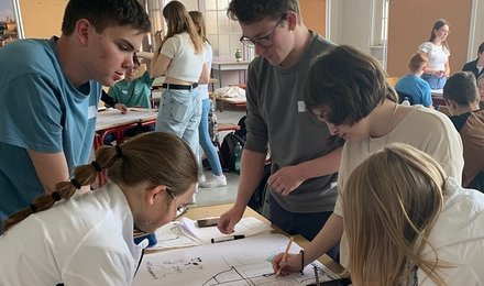 Schülerinnen und Schüler arbeiten in Gruppen an einem Plakat und zeichnen das Schulgebäude