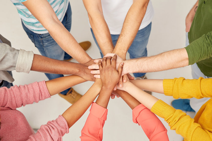 Mehrer Personen in unterschiedlich farbiger Kleidung legen in der Mitte ihre Hände übereinander