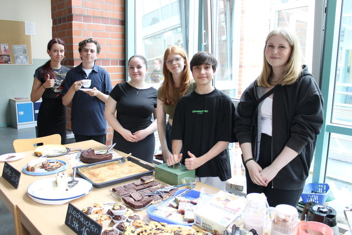 Schülerinnen und Schüler stehen hinter einem Kuchenverkaufsstand