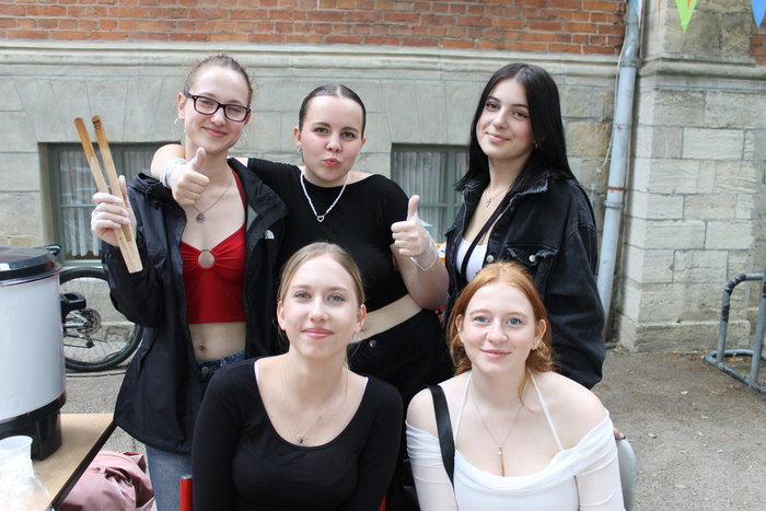 Fünf Schülerinnen lächeln in die Kamera. Eine hält eine Holzzange in der Hand und eine andere trägt Plastikhandschuhe